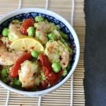 Ceramic bowl with colorful flowers on a sushi mat, filled with shrimp, tomatoes and edamame over rice.