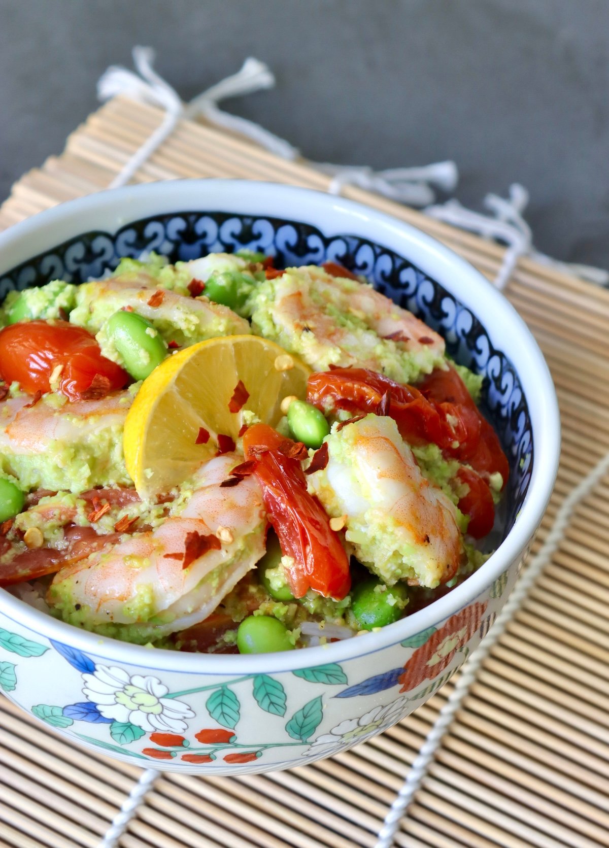 Sheet-Pan-Shrimp-with-Edamame-Pesto Ceramic bowl with colorful flowers, filled with shrimp, tomatoes and edamame over rice.