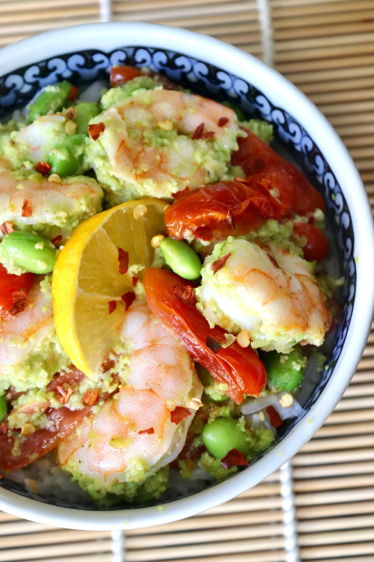 Sheet-Pan-Shrimp-with-Edamame-Pesto Top view of ceramic bowl with colorful flowers, filled with shrimp, tomatoes and edamame over rice.