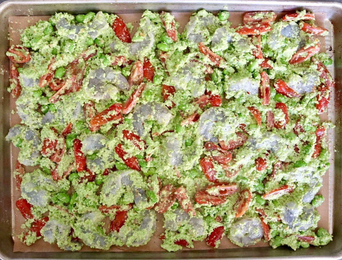 Sheet-Pan-Shrimp-with-Edamame-Pesto Sheet pan with an even layer of raw shrimp with edamame and sliced small tomatoes.