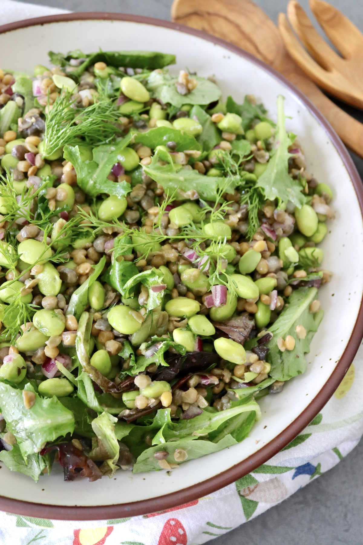 Top view, close up, of lentil and edamame salad in a large bowl with wooden servers next to it.