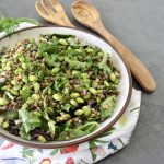 Top view of lentil and edamame salad in a large bowl with wooden servers next to it.