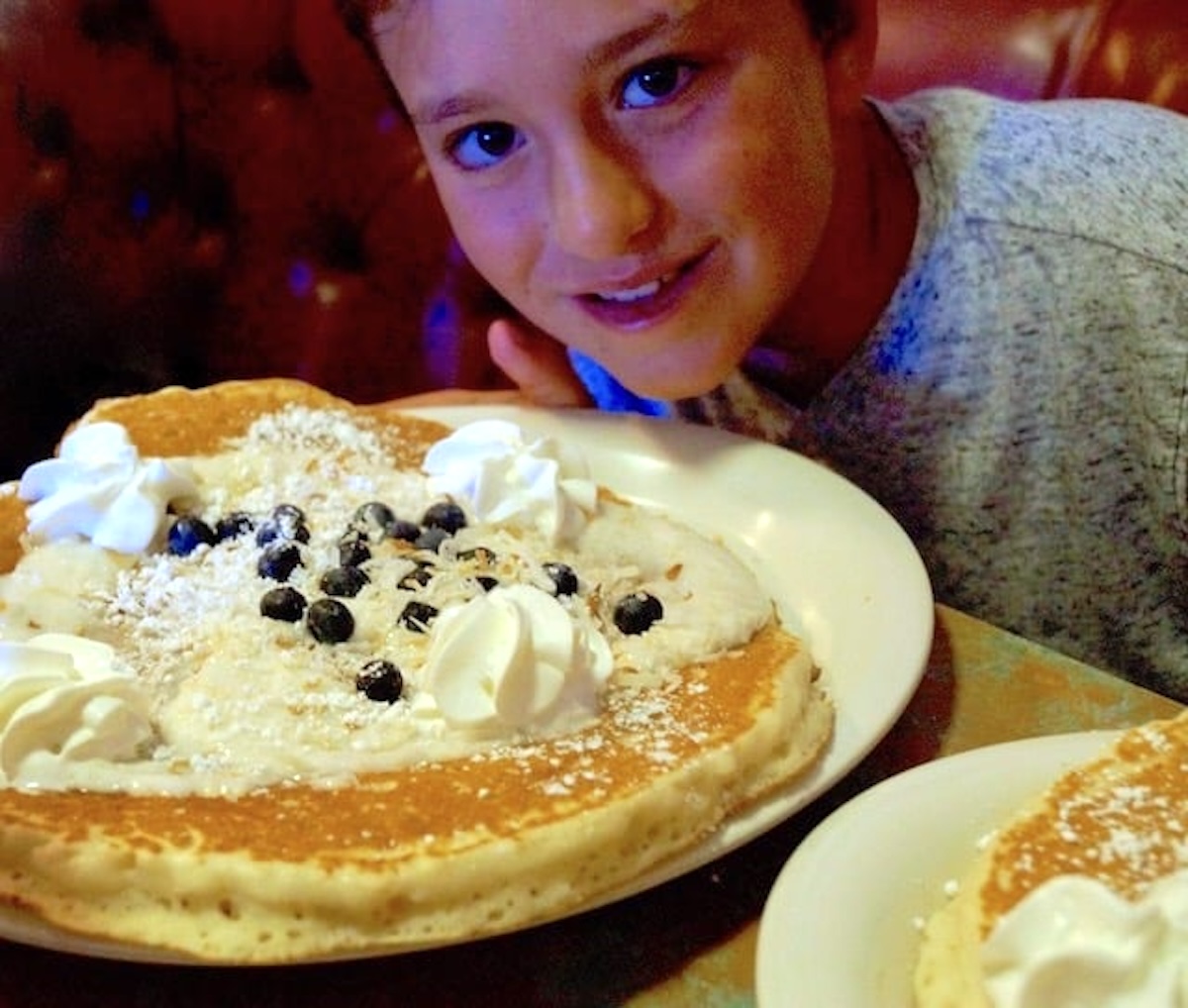 Giant pancakes on a while plate with whipped cream and chocolate chips, with cute young boy.