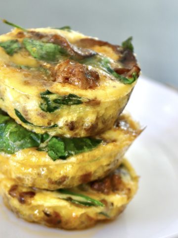 Three stacked egg bites with spinach and sausage, on a white plate.
