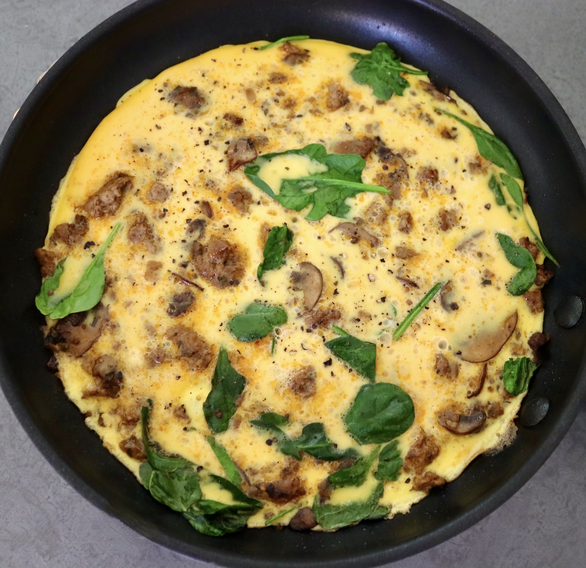 Frittata in black skillet with sausage and spinach.
