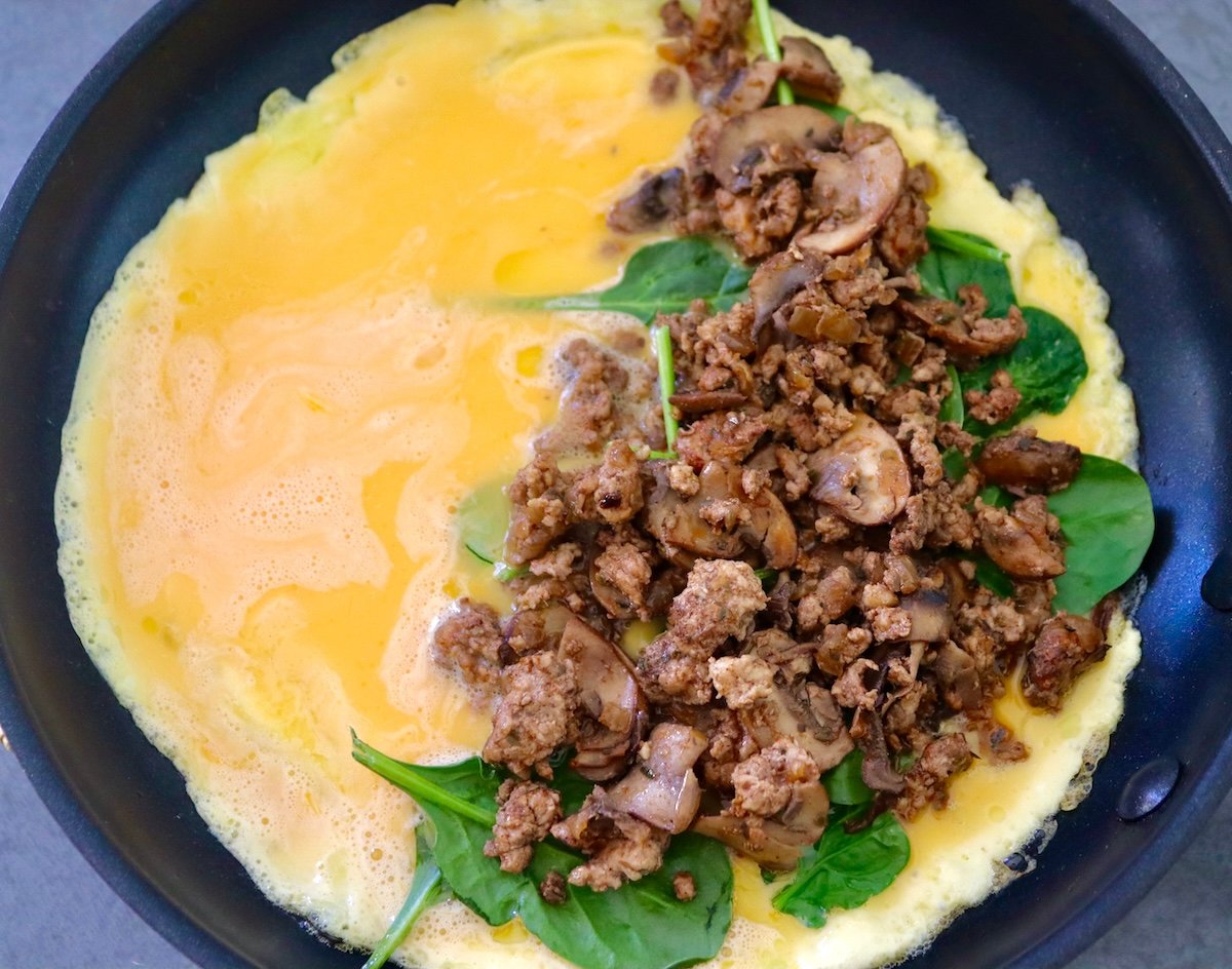 Omelet just before it's folded over sausage and spinach filling in a skillet
