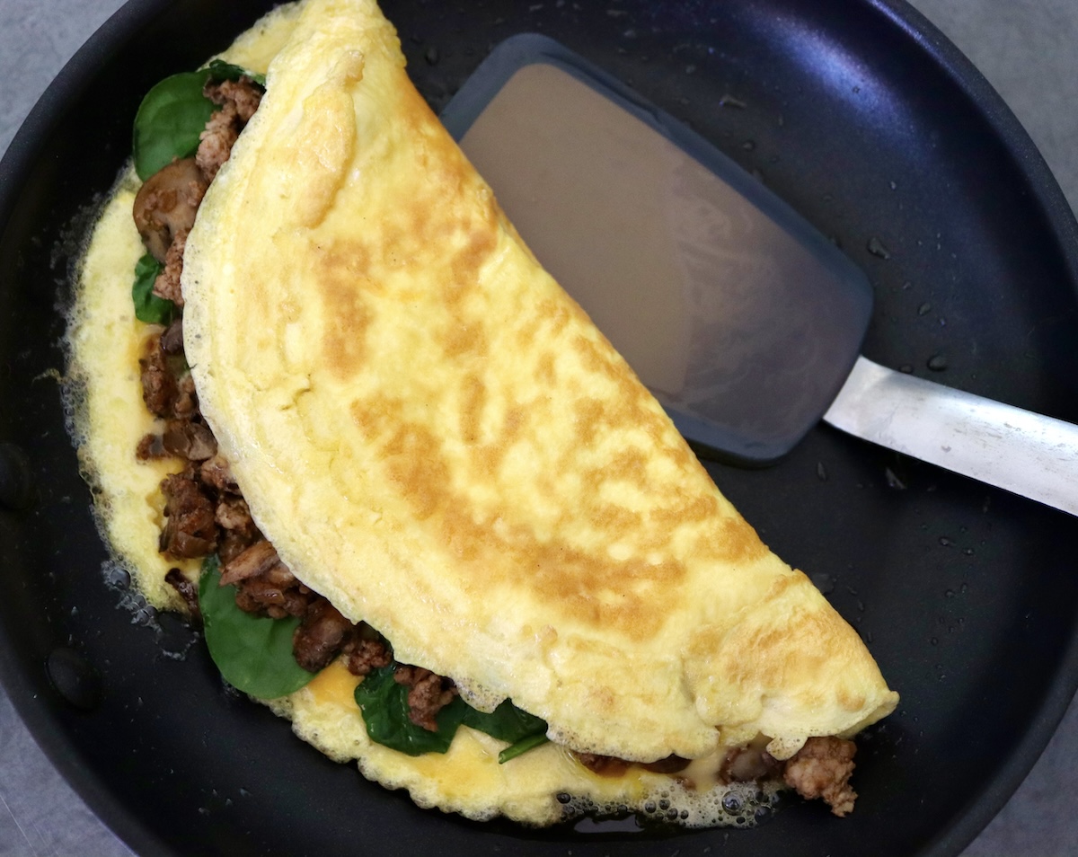 Omelet folded over sausage and spinach filling in a skillet with a silicon spatula.