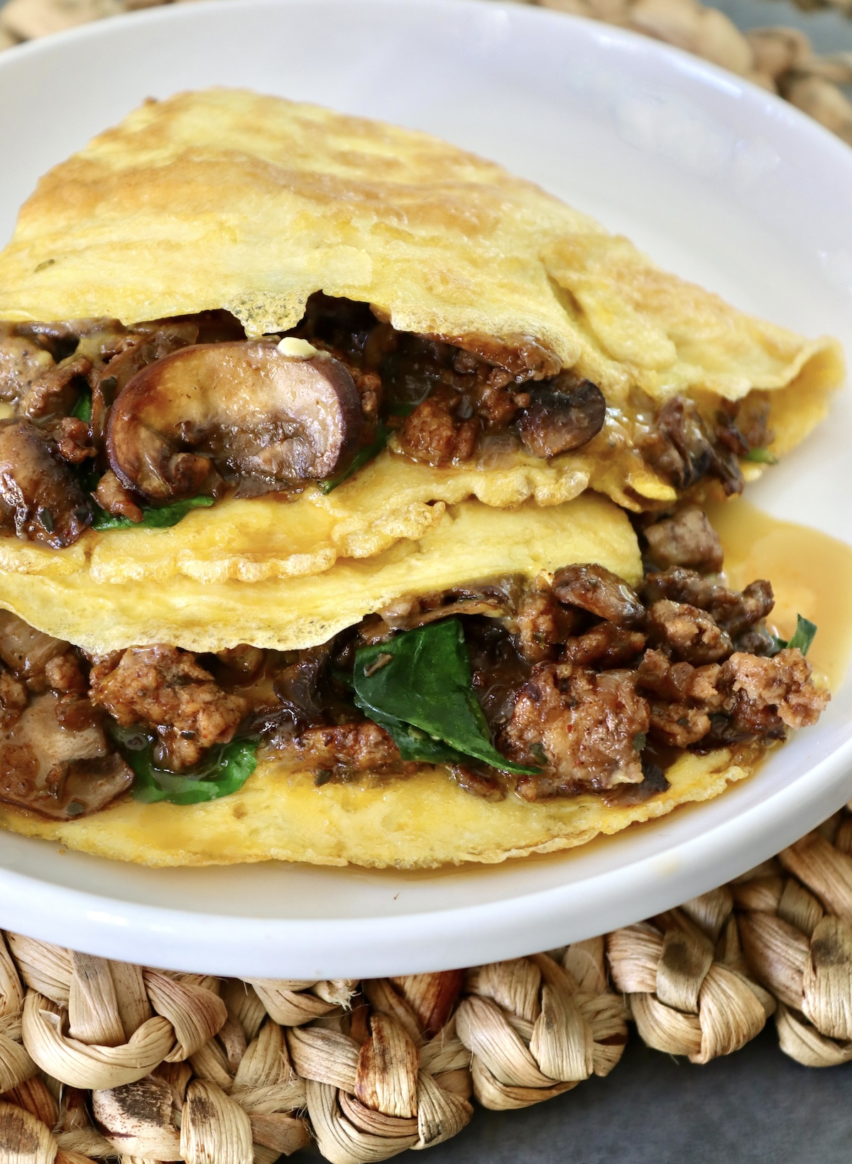 Two portions of an American folded omelet with sausage and spinach, on a white plate.