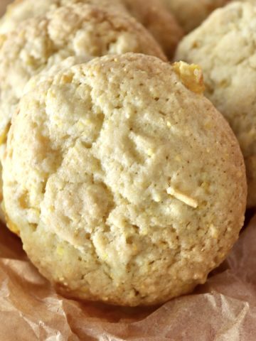 Close up of crispy, perfectly round, cornbread cookies, on parchment paper on a red and white cloth.