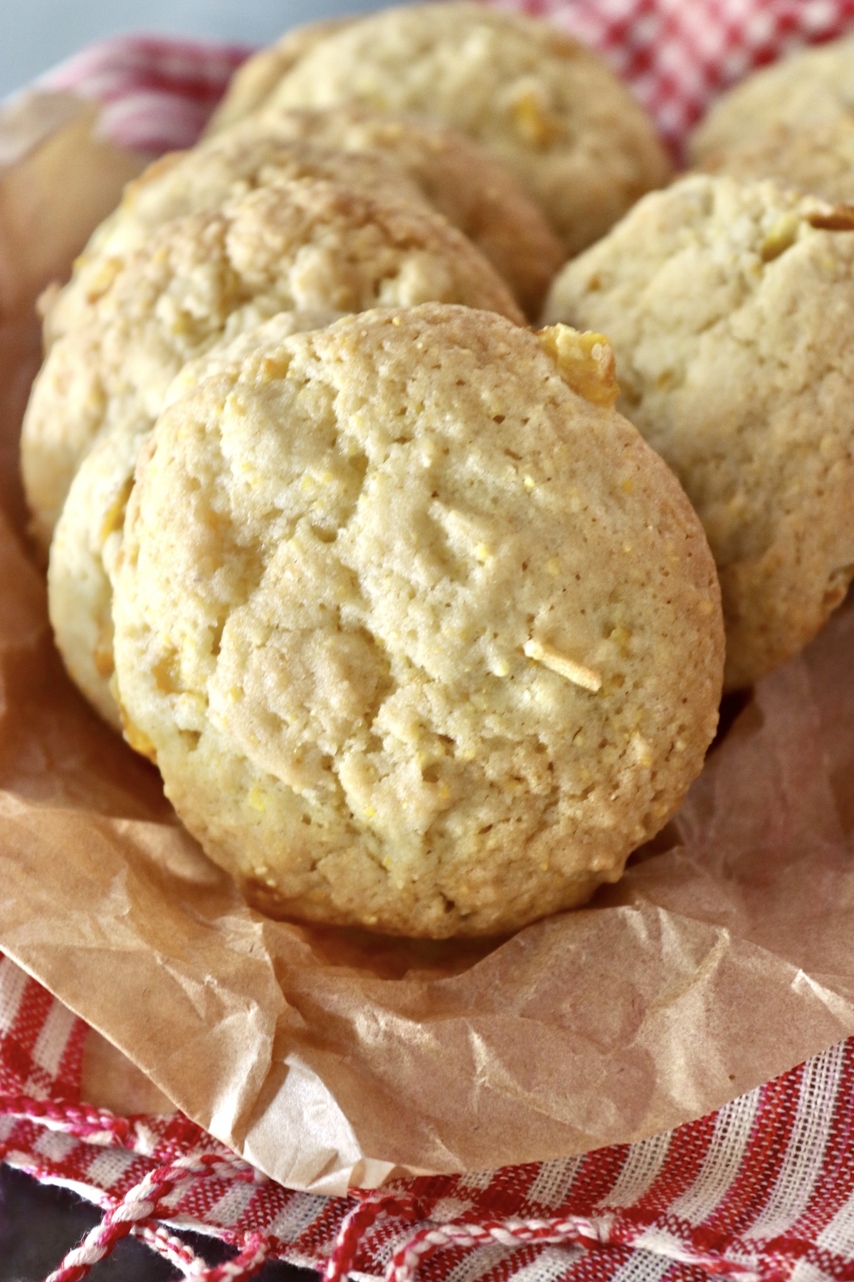 Close up of crispy, perfectly round, cornbread cookies, on parchment paper on a red and white cloth.