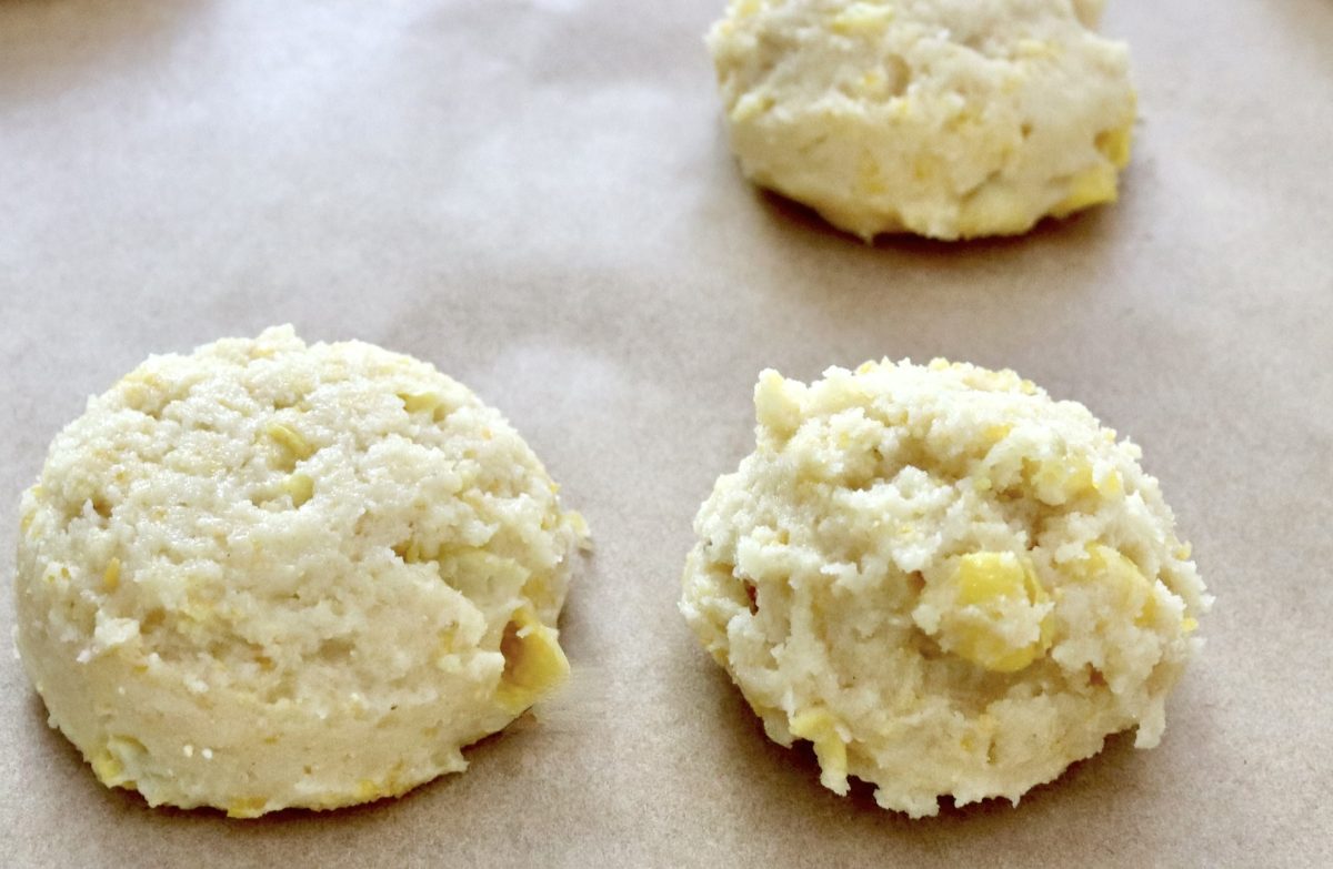 One flattened ball of corn cookie dough on parchment, and one rounded ball of cookie dough.