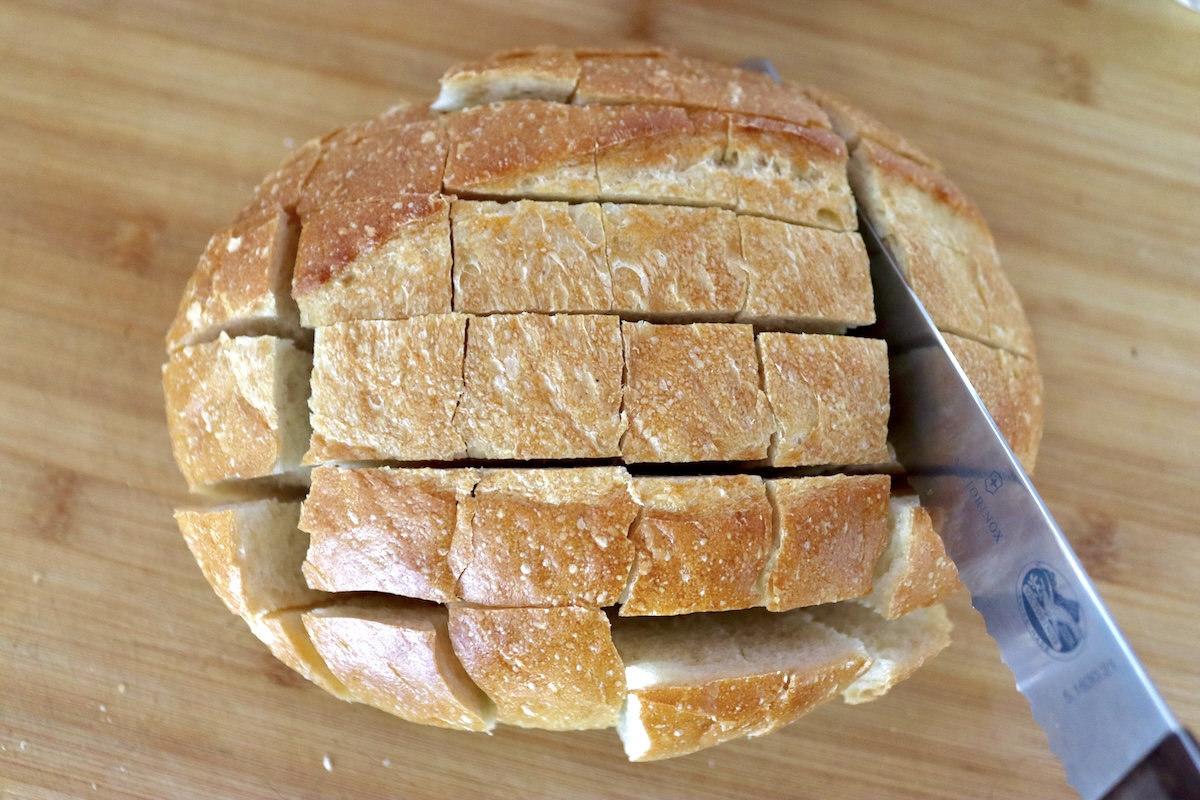 Pull-Apart French Toast Whole round loaf of French bread being cut into squares for pull apart french toast,.