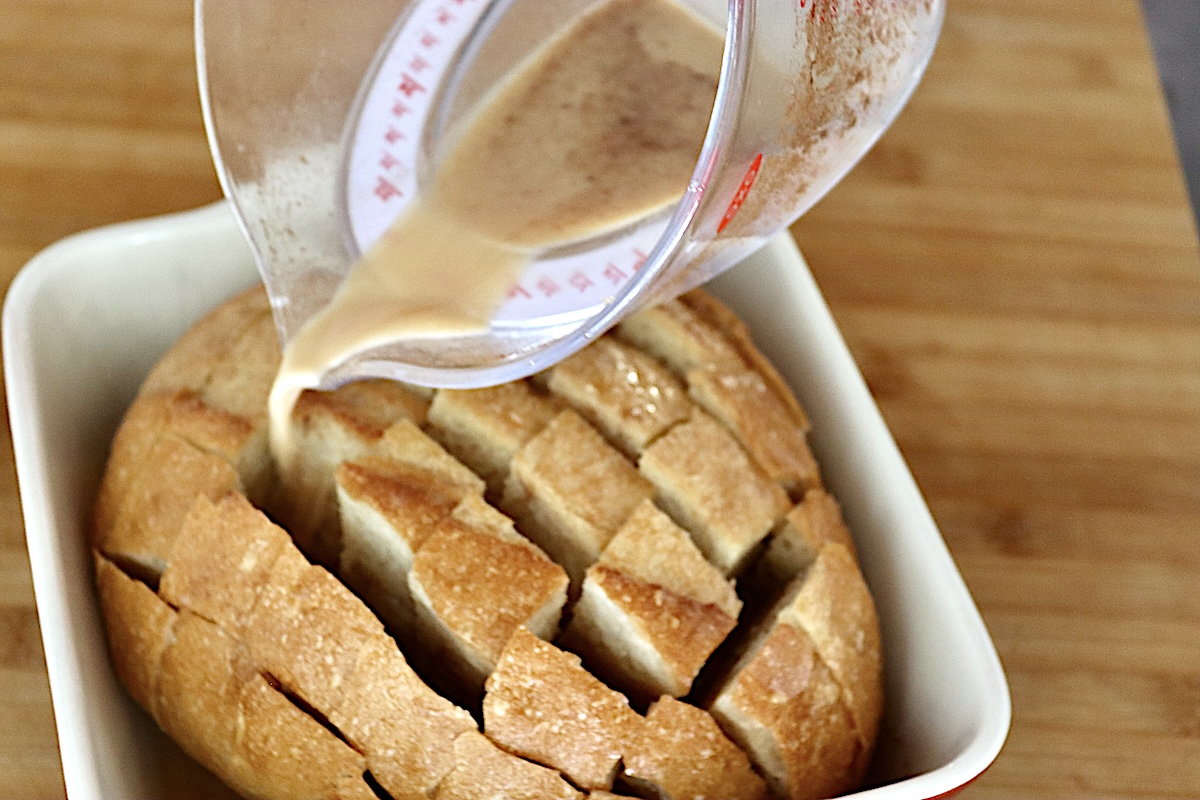 Pull-Apart French Toast French toast egg mixture being poured from a measuring cup into the cracks of the bread.