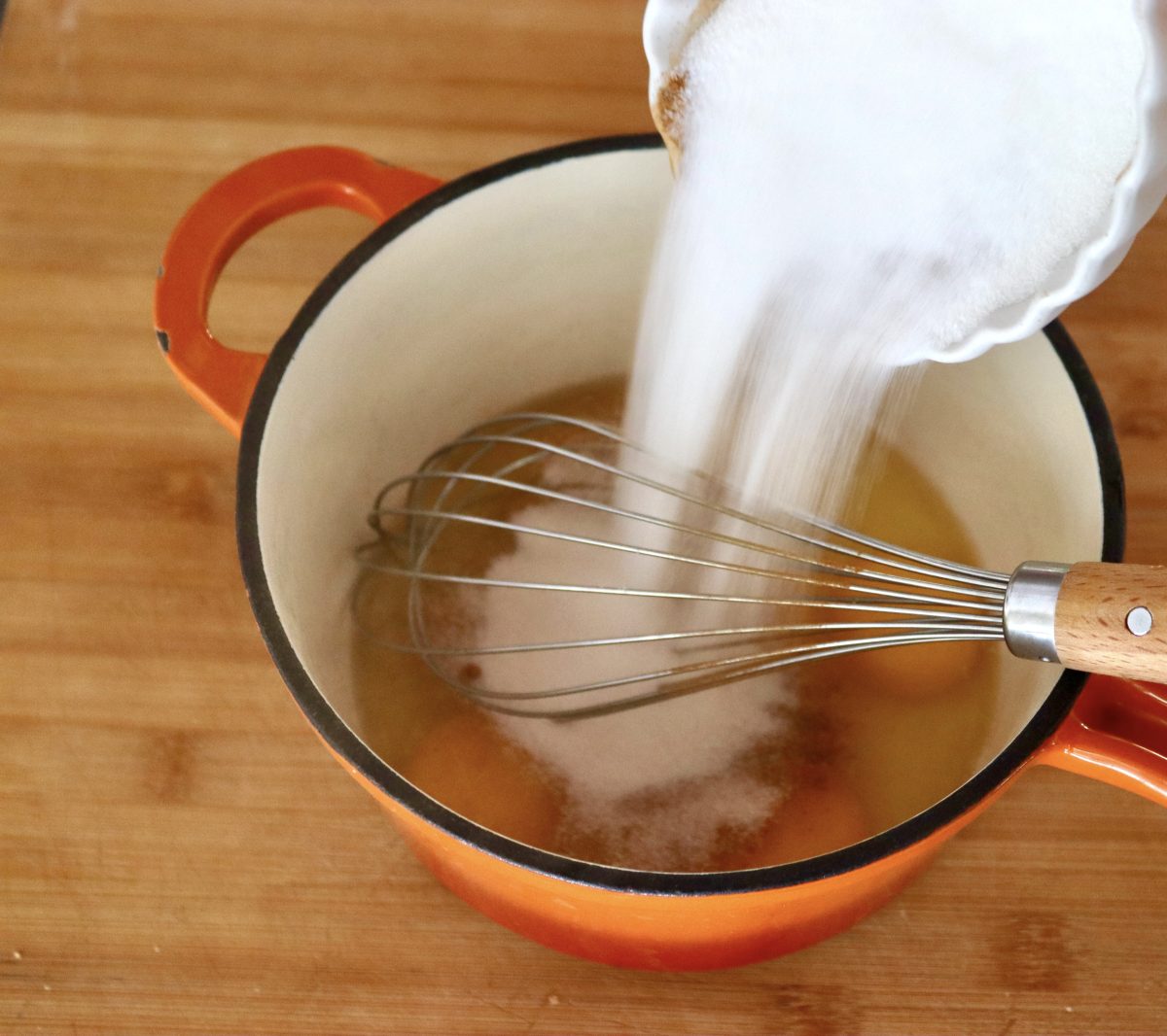 Pull-Apart French Toast White sugar being poured into an orange saucepan with eggs at the bottom.
