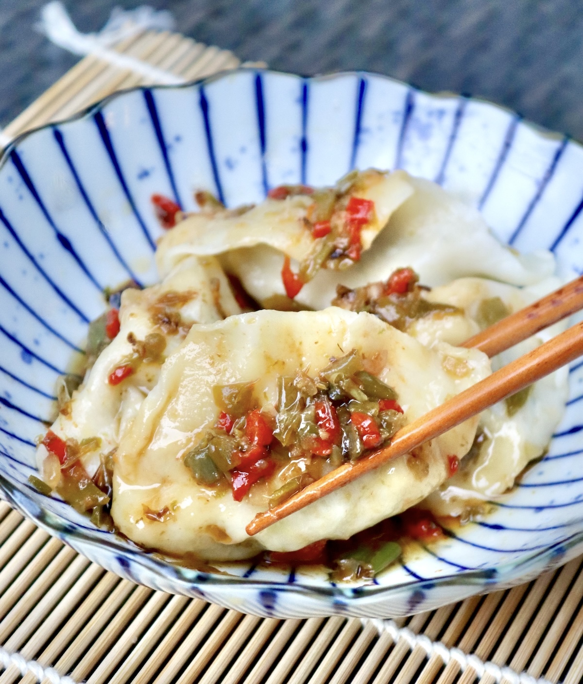 Shishito-Pepper-Salsa-Recipe Small blue and white striped plate with a few dumplings with shishito pepper salsa on top with chopsticks.