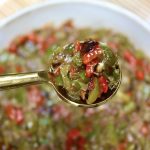Tiny gold spoon full with Shishito Pepper Salsa, being held over a bowl of it.
