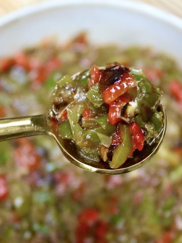 Tiny gold spoon full with Shishito Pepper Salsa, being held over a bowl of it.