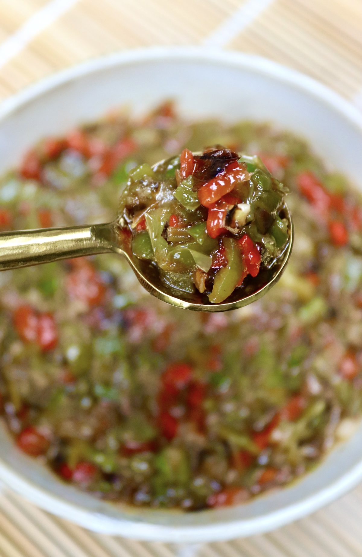 Tiny gold spoon full with Shishito Pepper Salsa, being held over a bowl of it.
