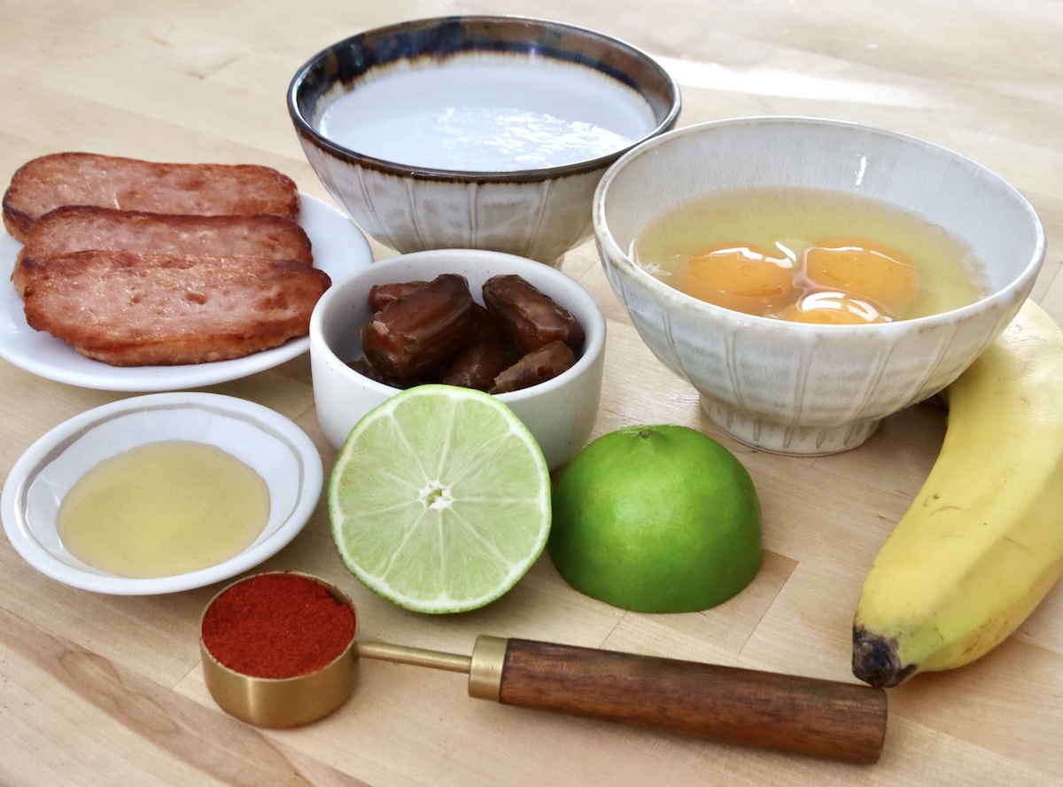 Halved lime, tablespoon of paprika, span slices, a few dates, eggs and coconut milk on a cutting board.