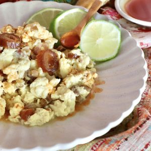 White plate with crispy spam in scrambled eggs, with three lime slices.
