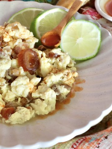 White plate with crispy spam in scrambled eggs, with three lime slices.