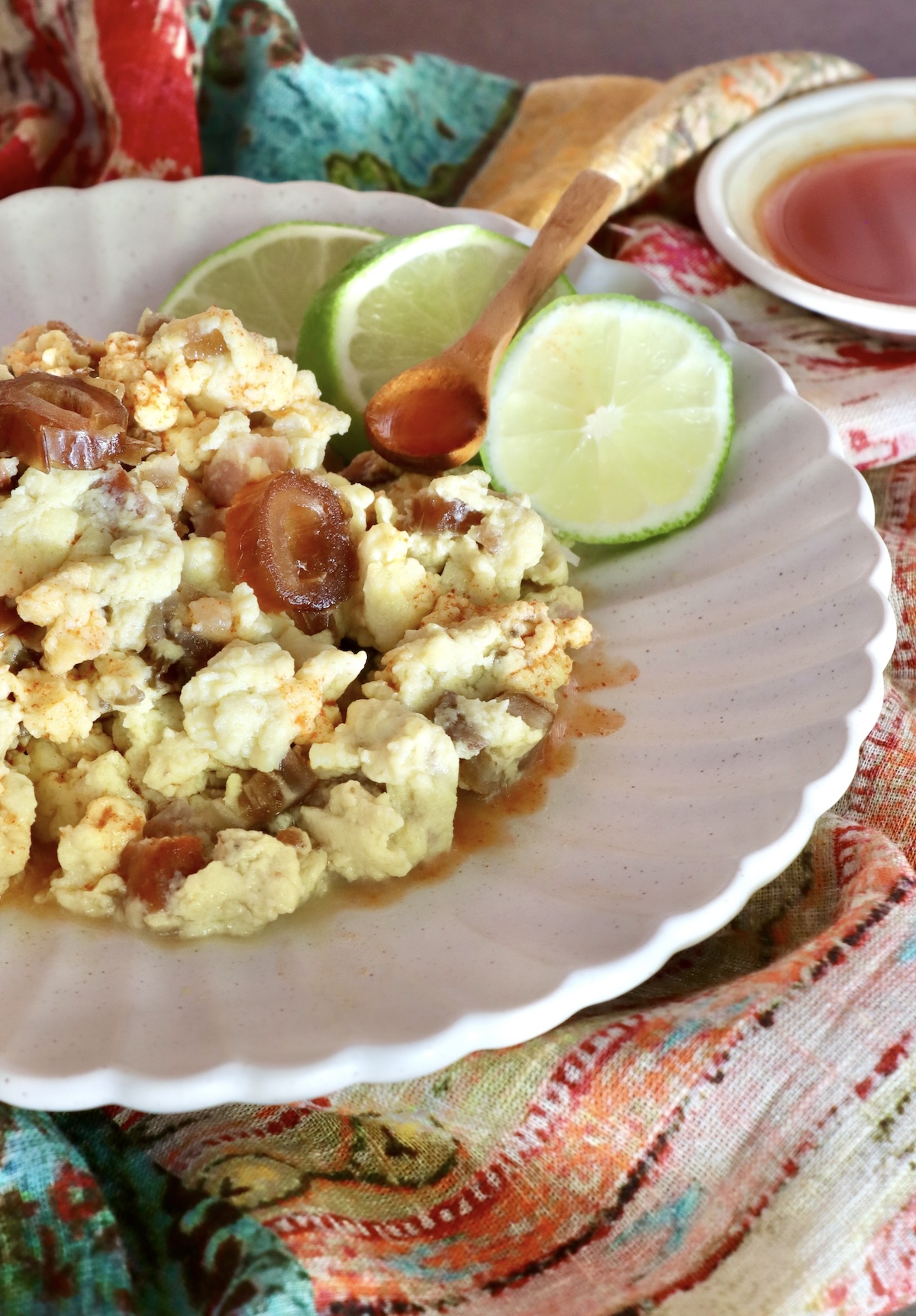 White plate with crispy spam in scrambled eggs, with three lime slices.