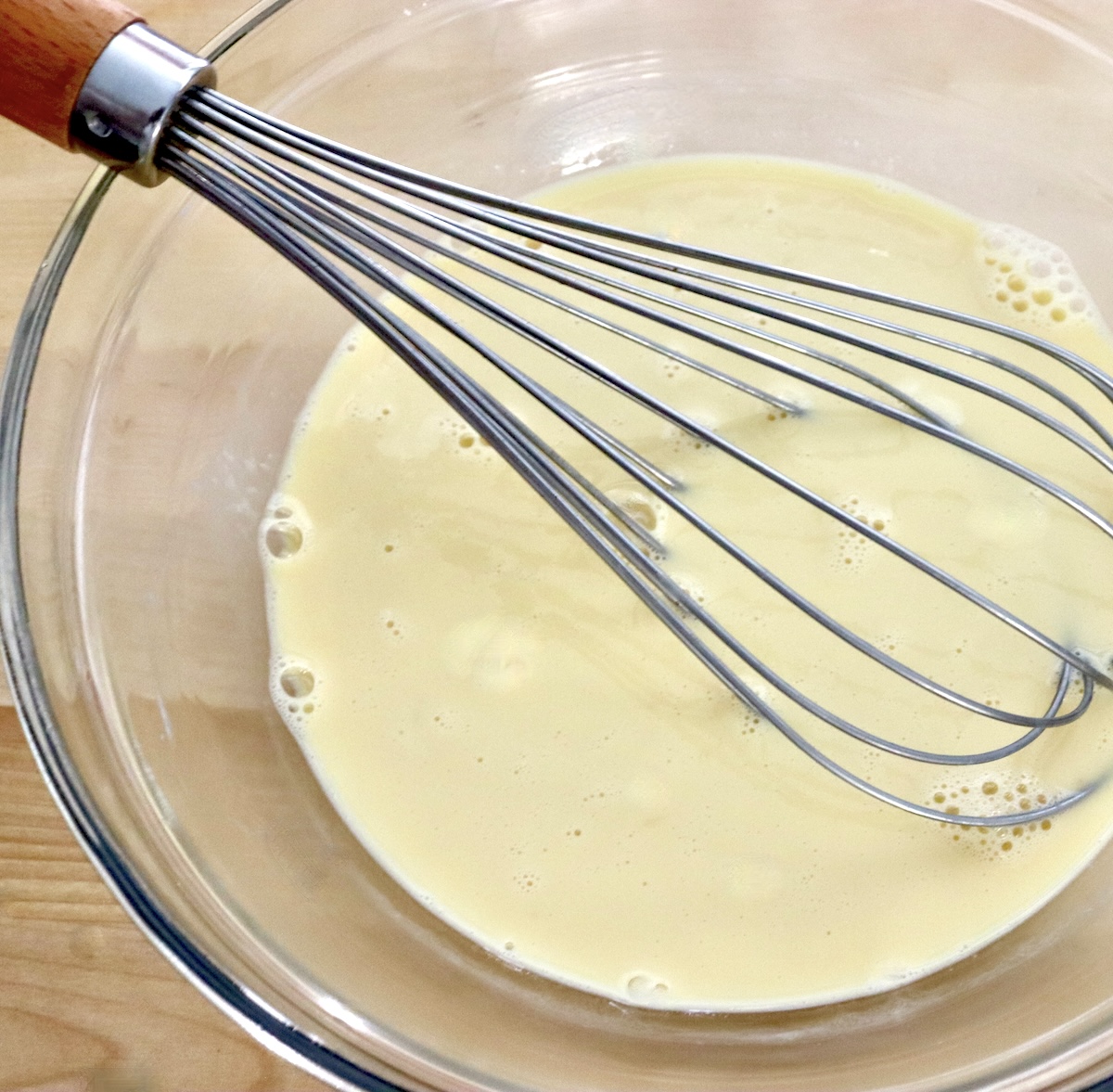 Glass bowl with whisked egg and coconut milk mixture.