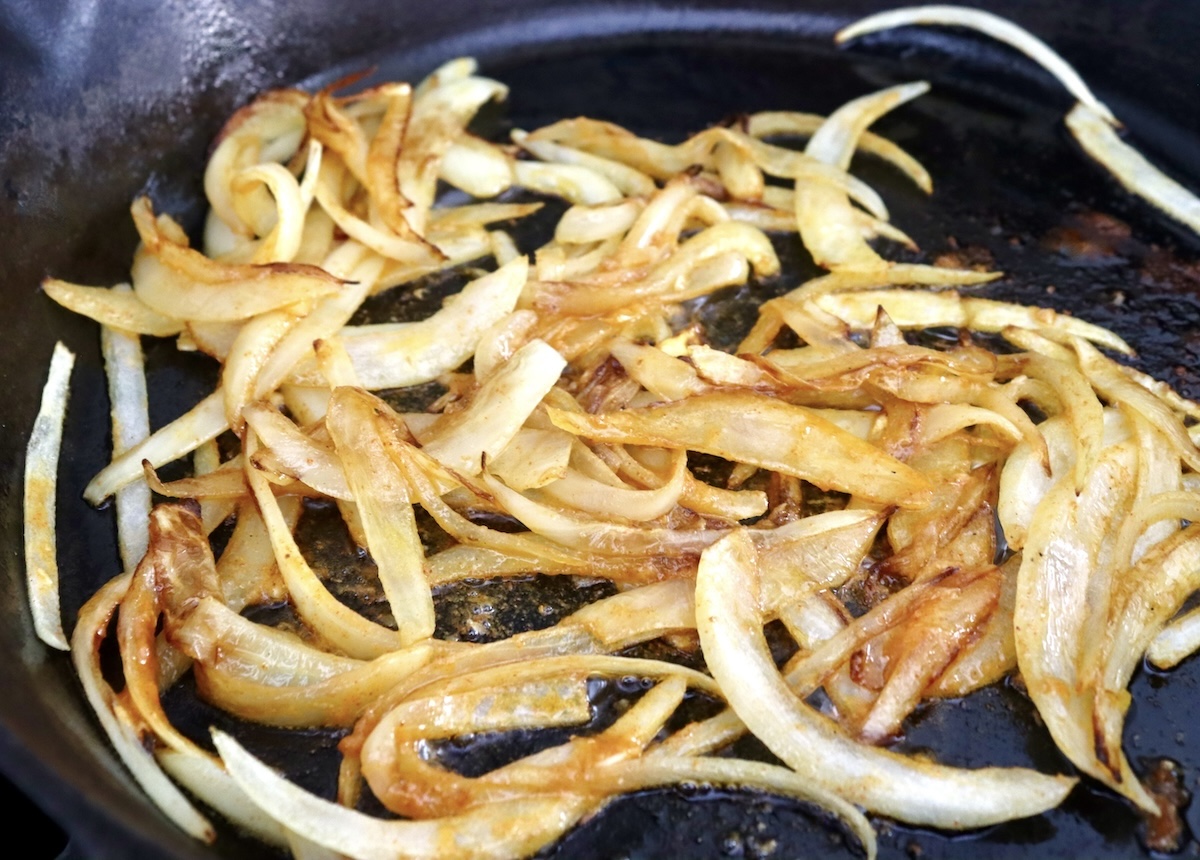 Whole-Cauliflower-One-Pan-Dinner-with-Tahini-Sauce Sautéed, sliced onions in a cast iron skillet.