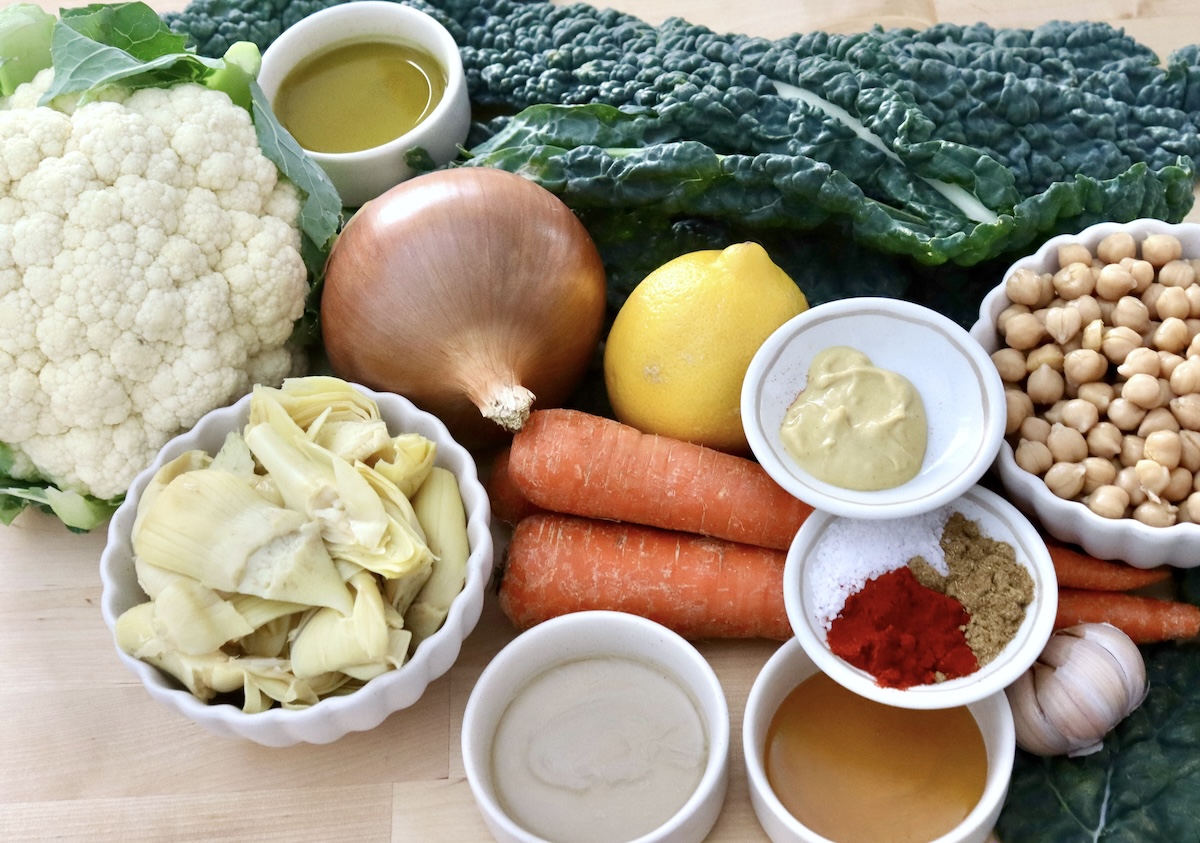 Whole-Cauliflower-One-Pan-Dinner-with-Tahini-Sauce Ingredients for cauliflower vegetarian dinner including Tuscan kale, artichoke hearts, onion, carrots, lemon, olive oil, tahini, honey, mustard and spices.