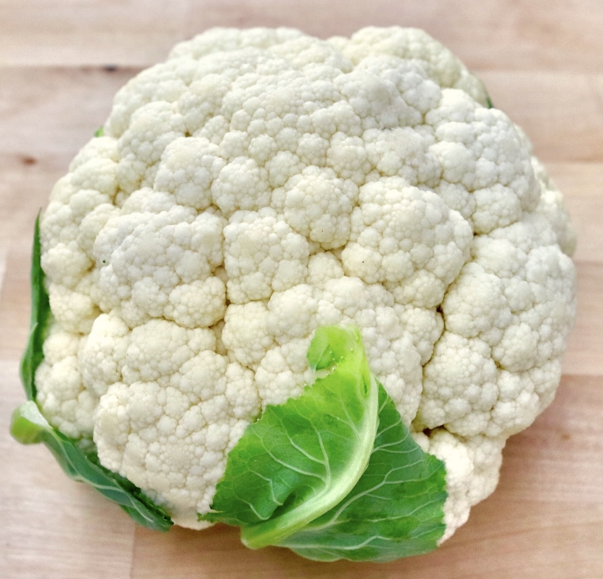 Whole-Cauliflower-One-Pan-Dinner-with-Tahini-Sauce whole head of cauliflower with a couple of bright green leaves.