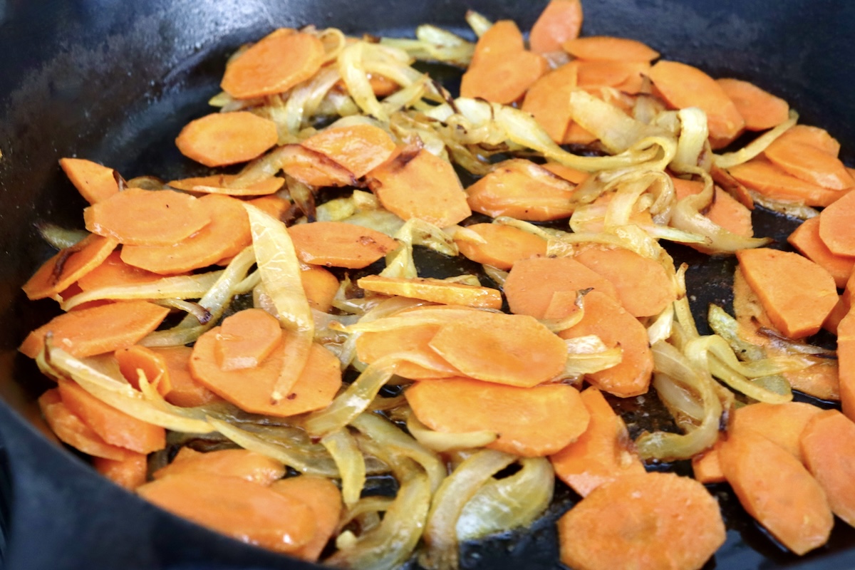 Whole-Cauliflower-One-Pan-Dinner-with-Tahini-Sauce Sautéed, sliced onions and carrots in a cast iron skillet.
