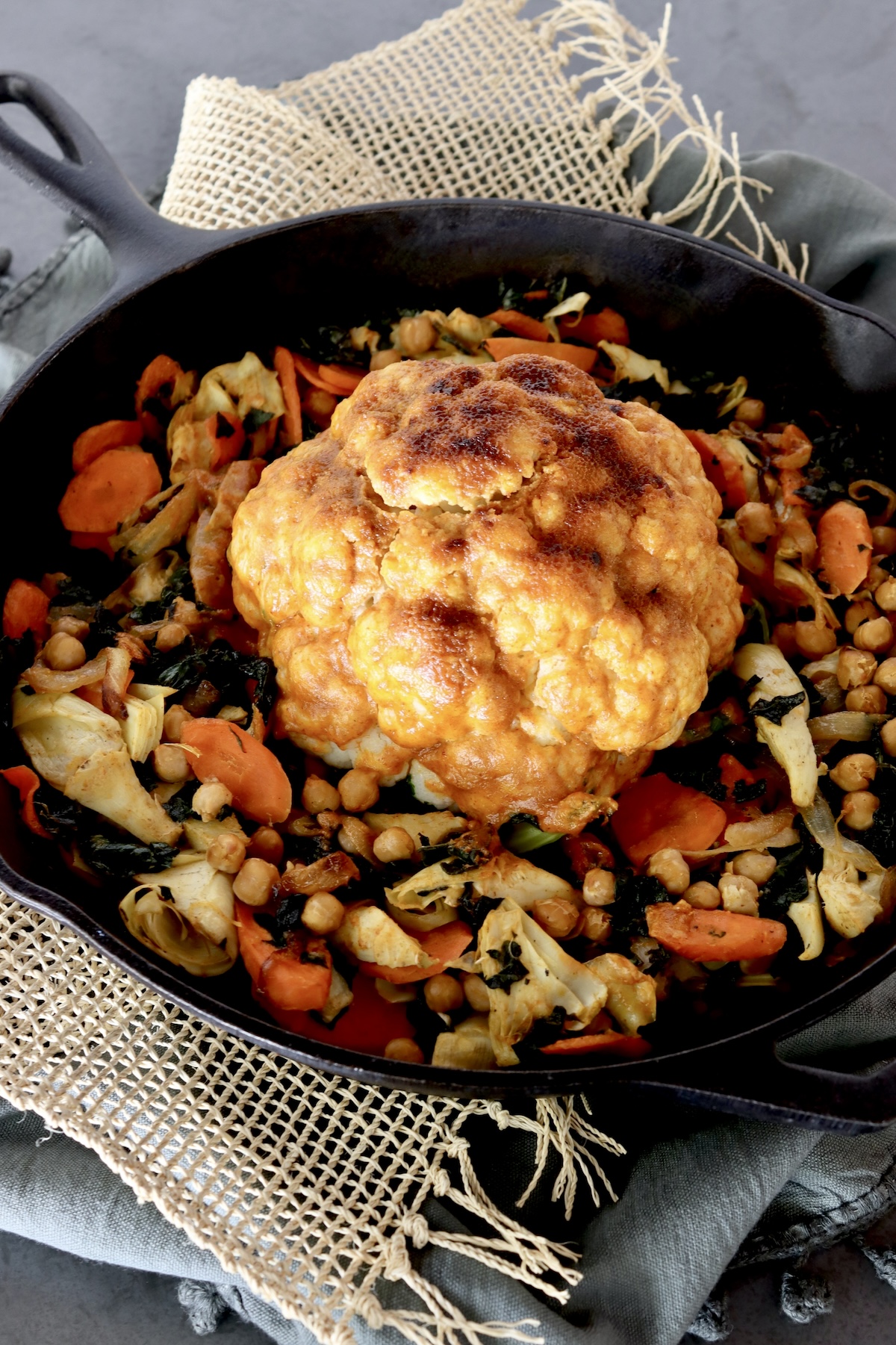 Whole cauliflower with red sauce in the center of a cast iron skillet with other vegetables.