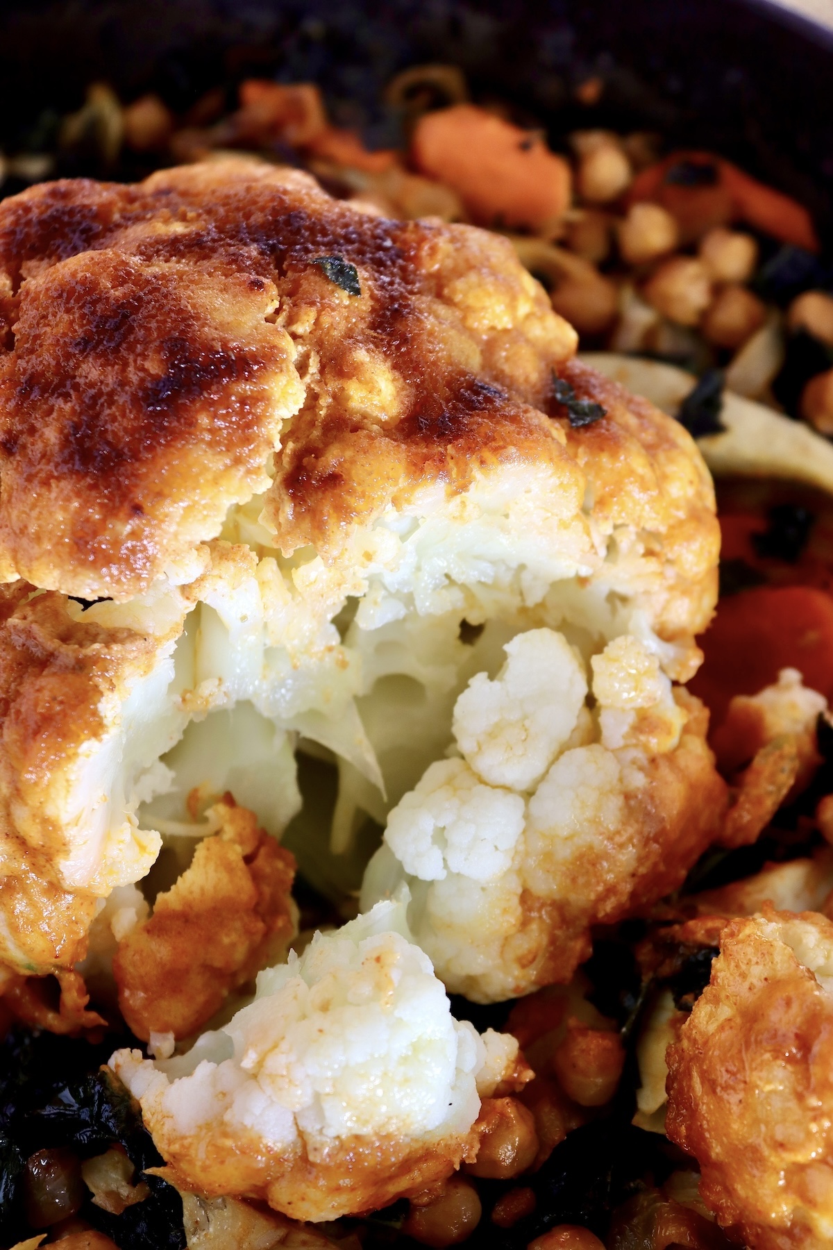 Whole-Cauliflower-One-Pan-Dinner-with-Tahini-Sauce Whole, tahinni sauce-coated, broiled cauliflower with a big piece cut off to reveal its white center.