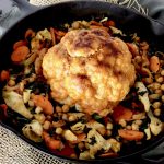 Whole cauliflower with red sauce in the center of a cast iron skillet with other vegetables.