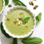 Top view of pistachio soup in a white crimp-edged bowl with mint leaves.