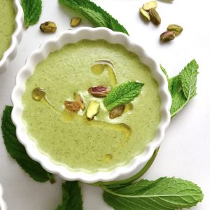 Top view of pistachio soup in a white crimp-edged bowl with mint leaves.