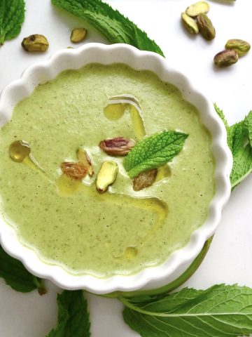 Top view of pistachio soup in a white crimp-edged bowl with mint leaves.