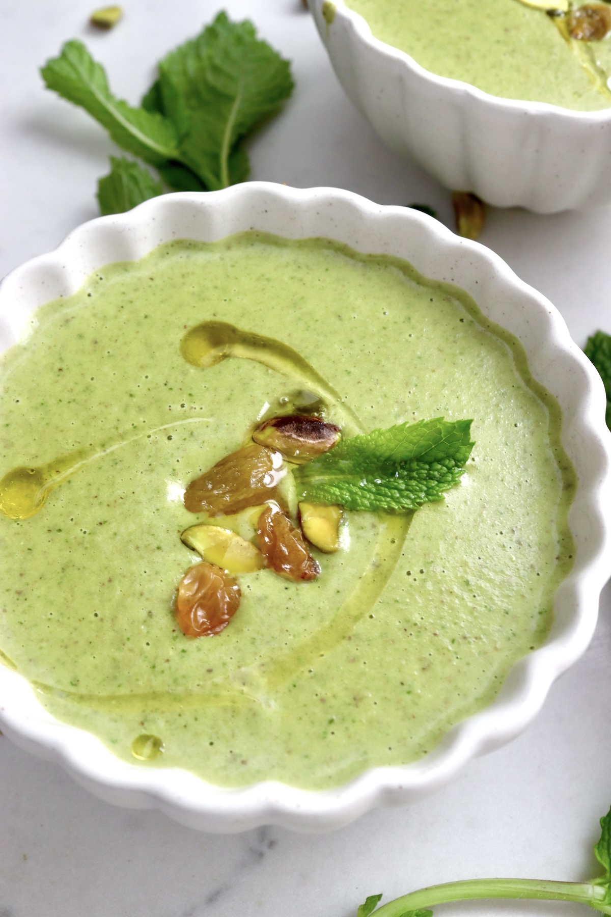 Close up, top view of pistachio soup in a white crimp-edged bowl with mint leaves.