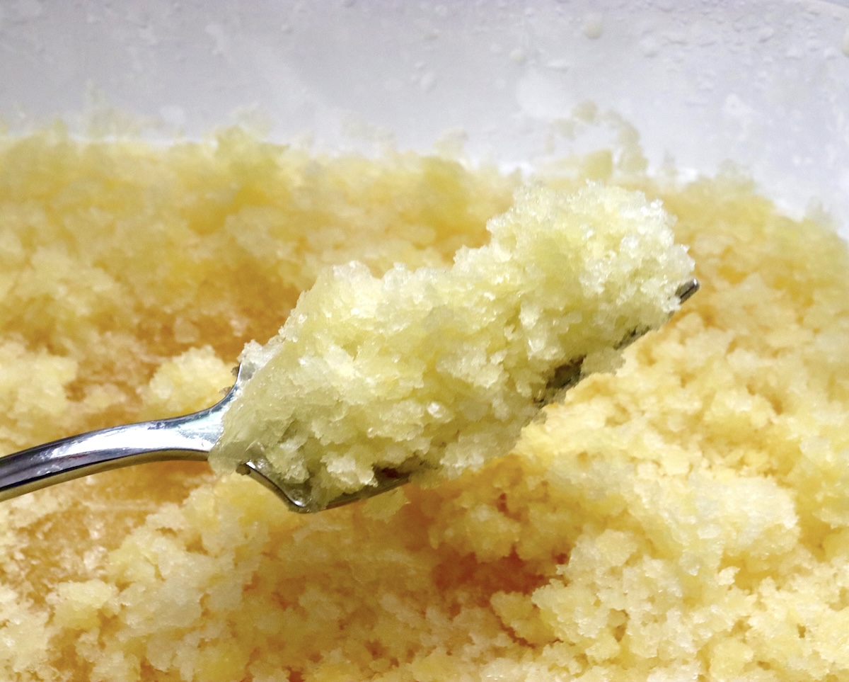 Frozen-Mimosa Plastic container filled with Orange Granita/Frozen Mimosa, with one bit being help up in a fork.