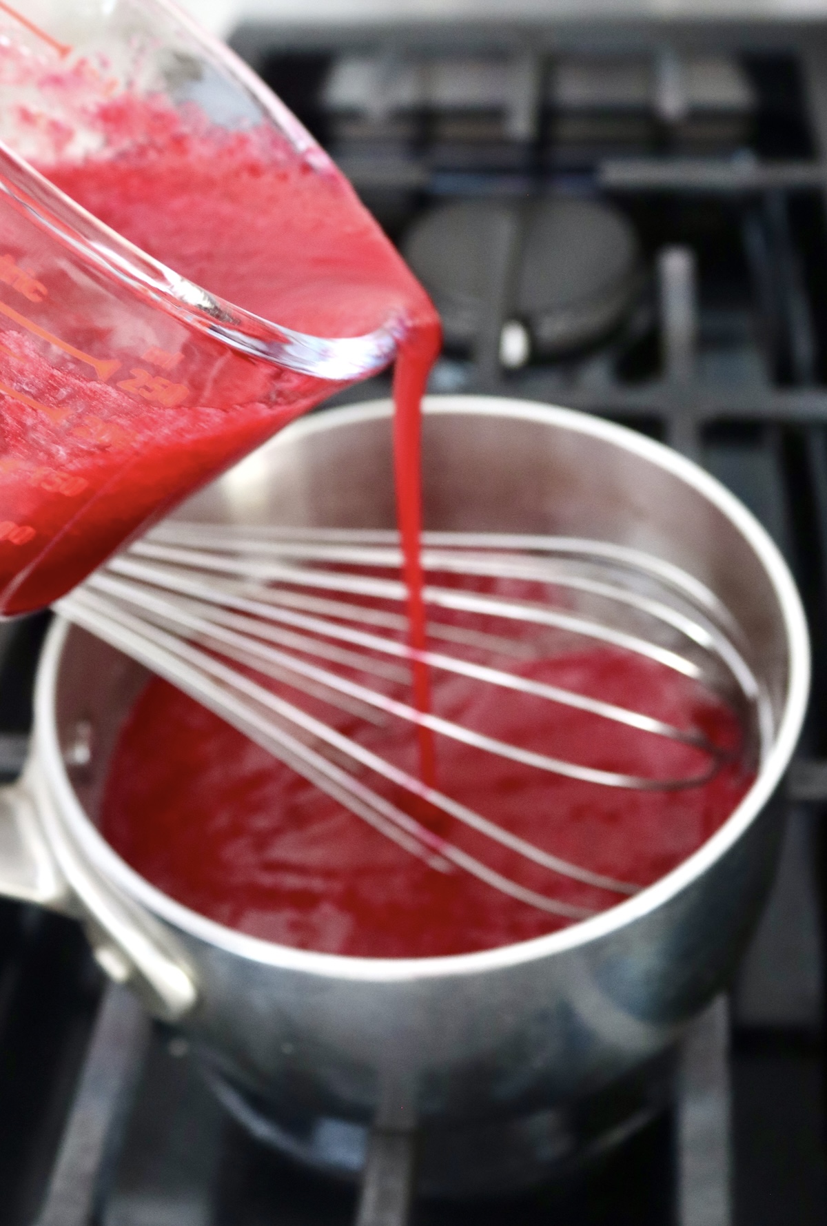 Small saucepan with prickly pear syrup and a whisk.