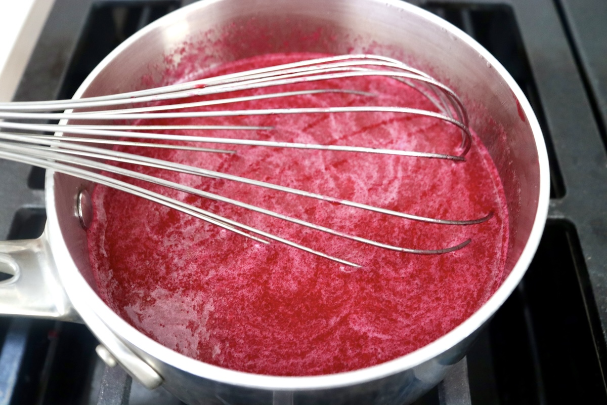 Small saucepan with prickly pear syrup and a whisk, whisking.