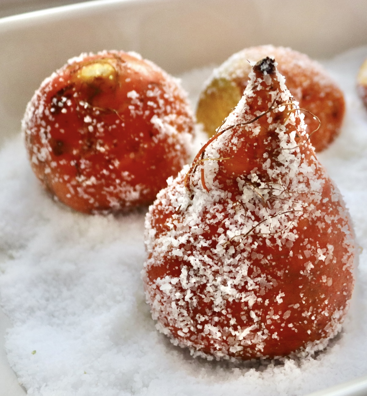 Three golden beets covered with a sprinkling of salt in a baking pan, sitting on top of a thick layer of salt.