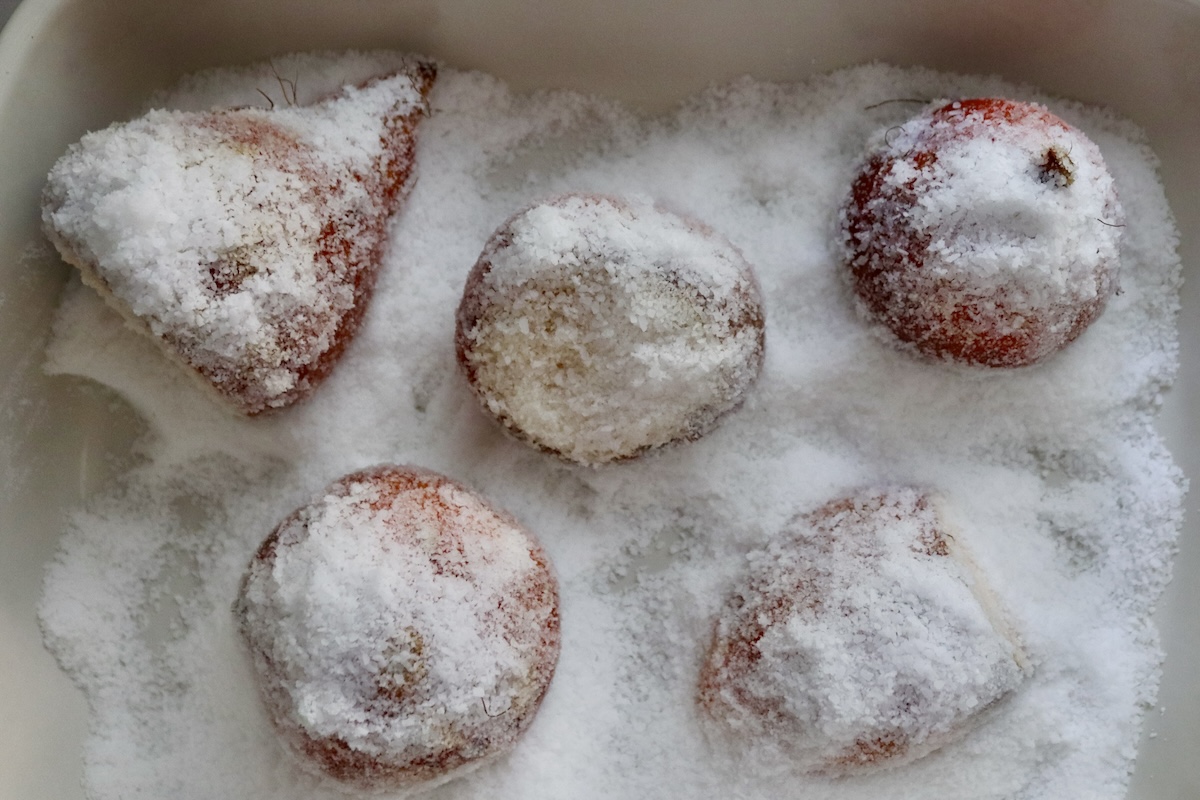 Golden beets covered with a generous amount of salt in a baking pan, sitting on top of a thick layer of salt.