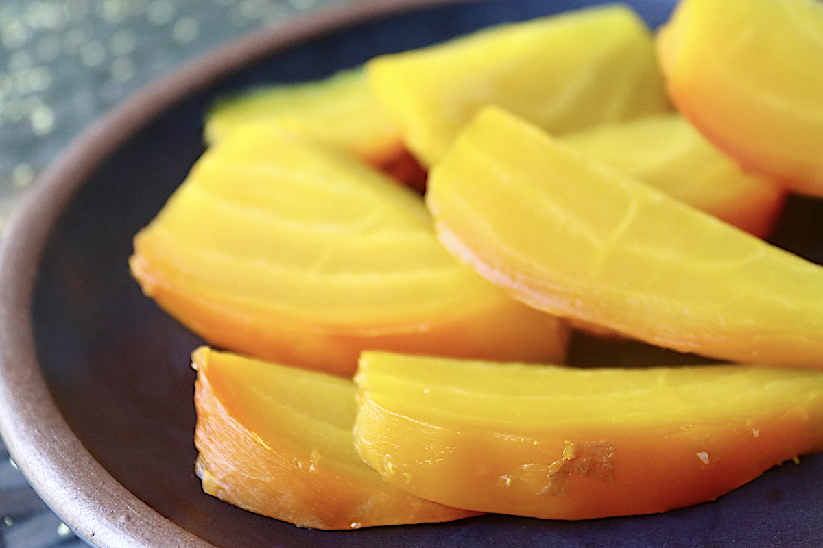 Sliced golden beets on a black plate.